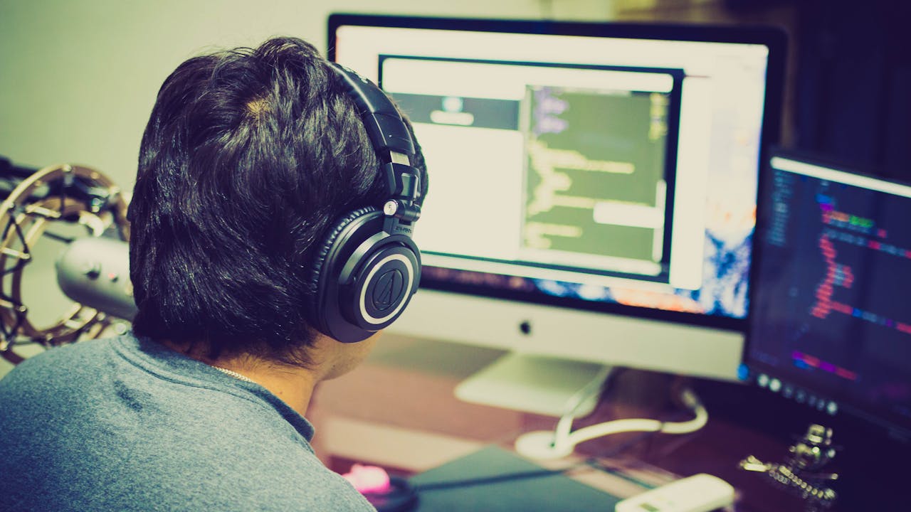 our-story A programmer with headphones focuses on coding at a computer setup with dual monitors.