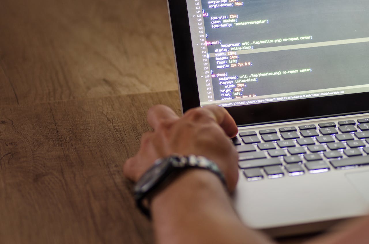 get-in-touch A developer's hand interacting with code on a laptop screen in a workspace setting.